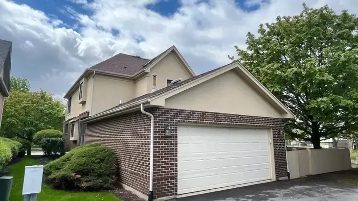 Suburban two-story house with brick and beige siding, white garage door, and cloudy sky