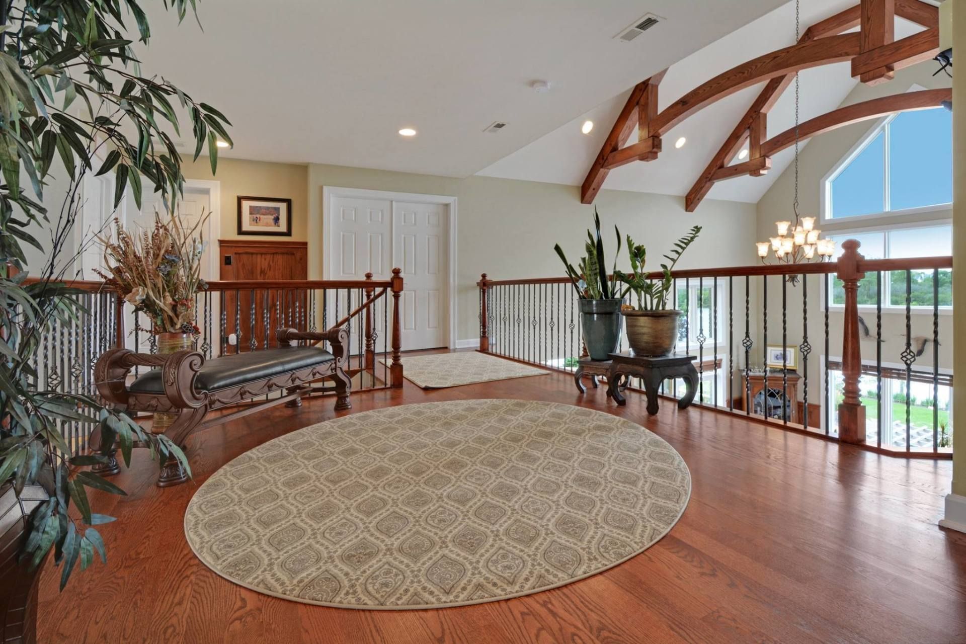 Spacious living area with wood floors, round rug, balcony railing, and vaulted ceiling beams