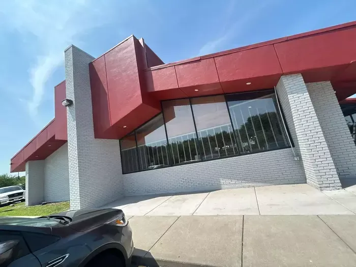 Red-and-white modern building with large windows and a sidewalk in front