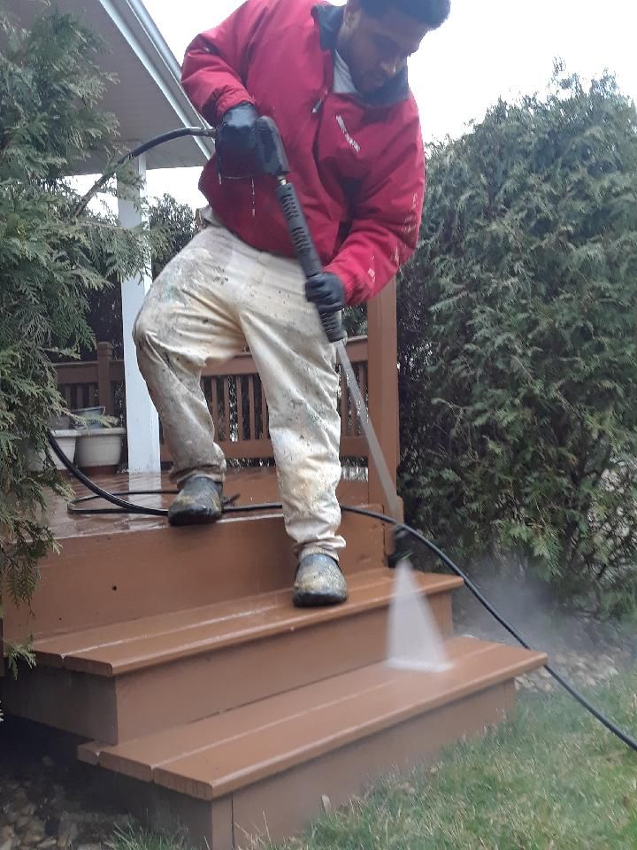 Person in red jacket pressure-washing brown porch steps with a black hose.