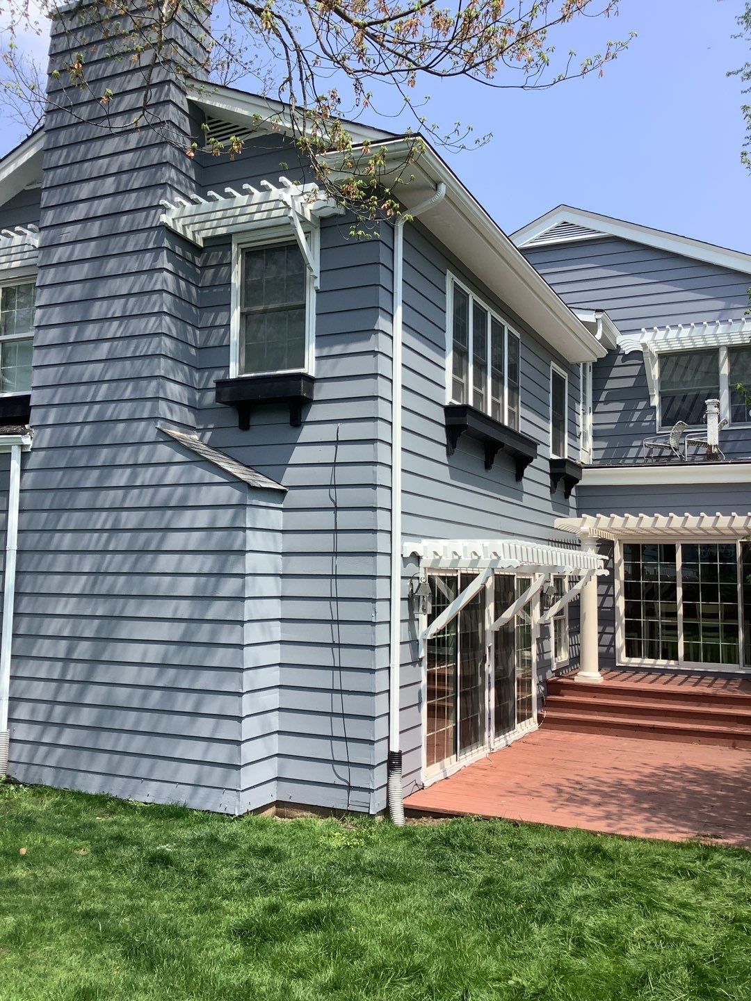 Blue-gray house exterior with a red brick patio, white trim, and sloped roof.