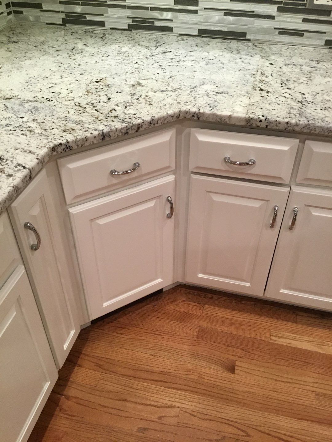 Corner kitchen cabinets with white doors, granite countertop, and hardwood floor