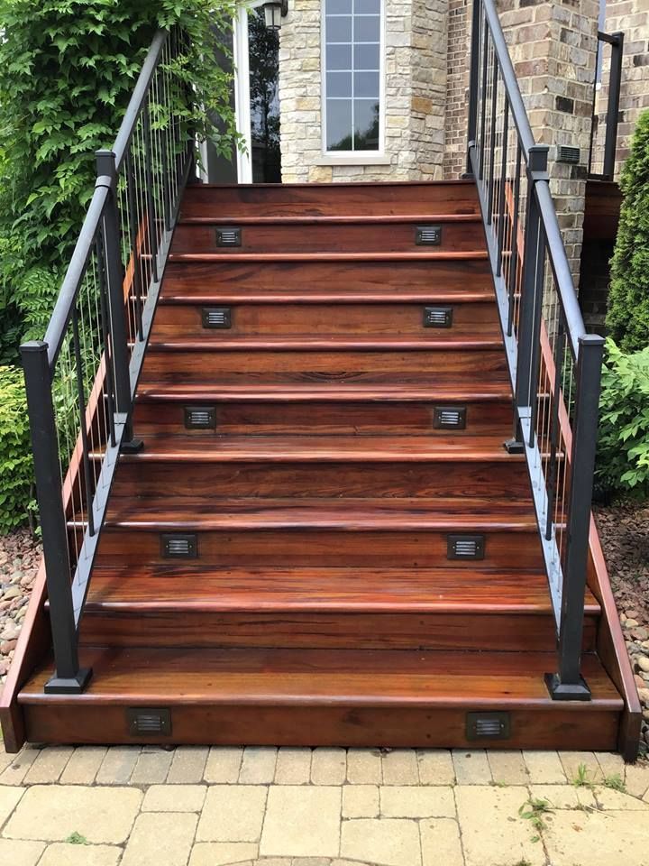 Front steps with dark wood stairs, black railings, and a stone house entrance.