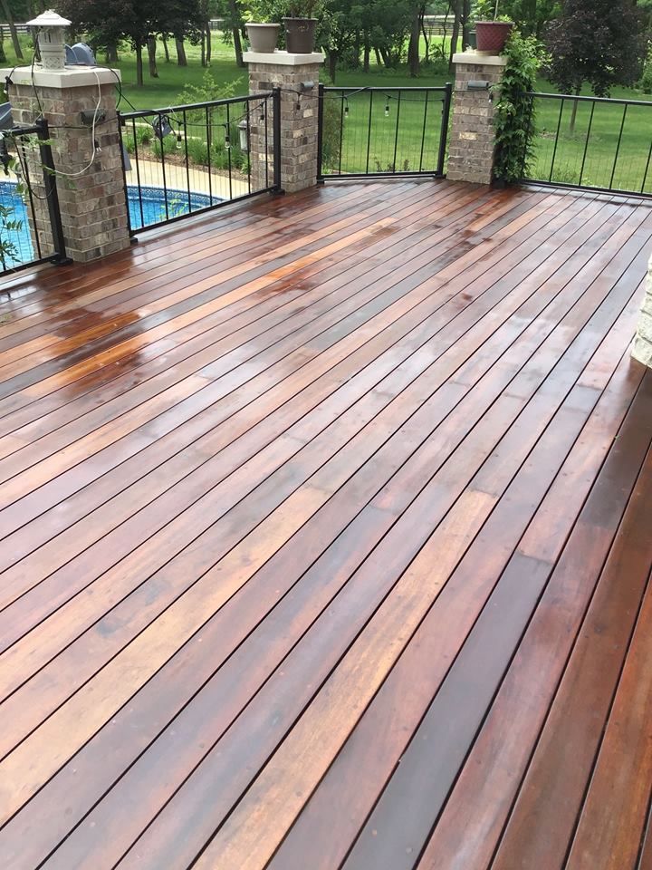 Wet wooden deck with stone pillars and black metal railing overlooking a green yard