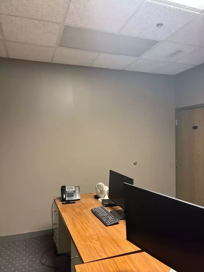Empty office with a wooden desk, computer monitors, keyboard, and gray walls under ceiling tiles
