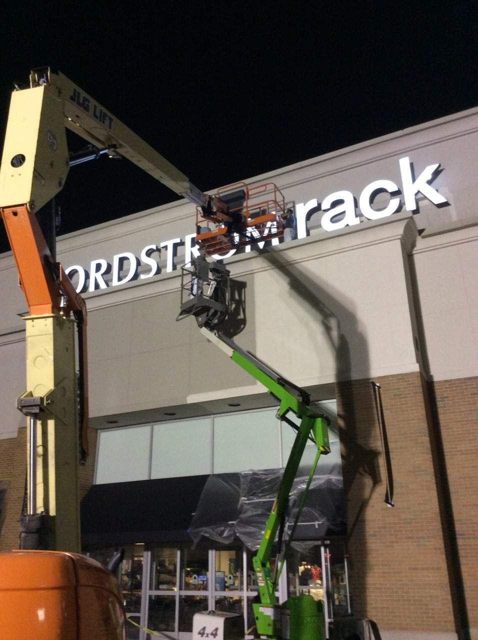 Two boom lifts working on the Nordstrom Rack sign at night