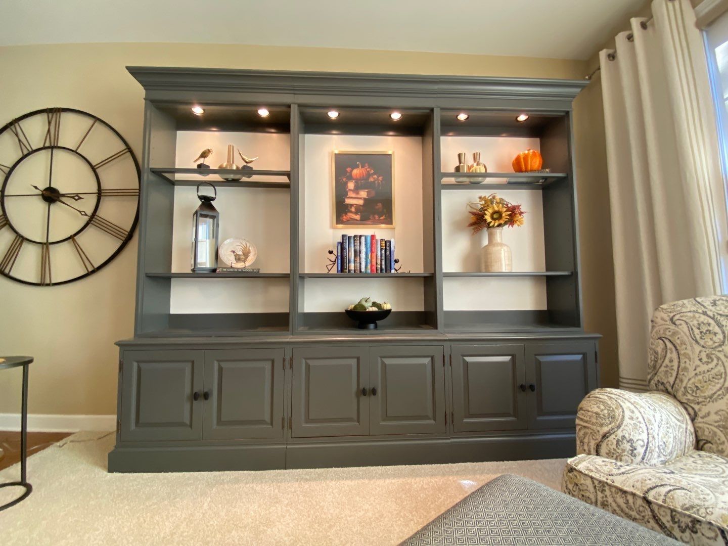 Built-in gray cabinet with shelves, decor, and wall clock in a bright living room