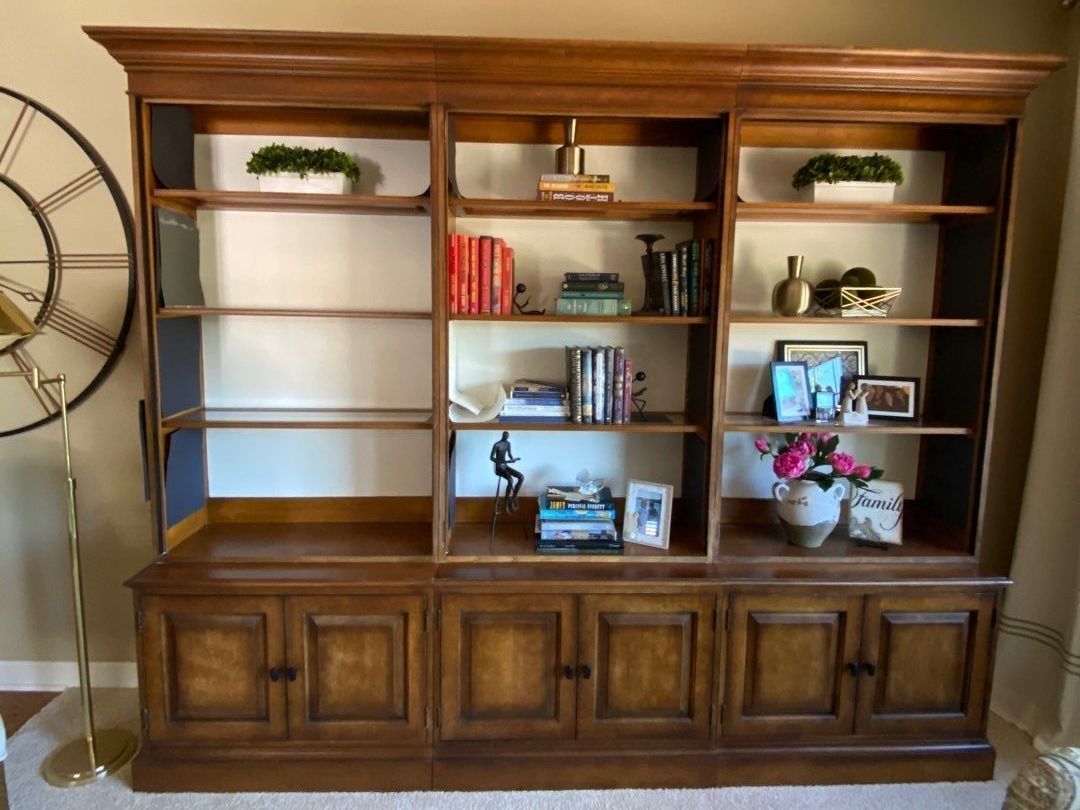 Wooden wall bookcase with shelves, books, decor, and flowers in a living room