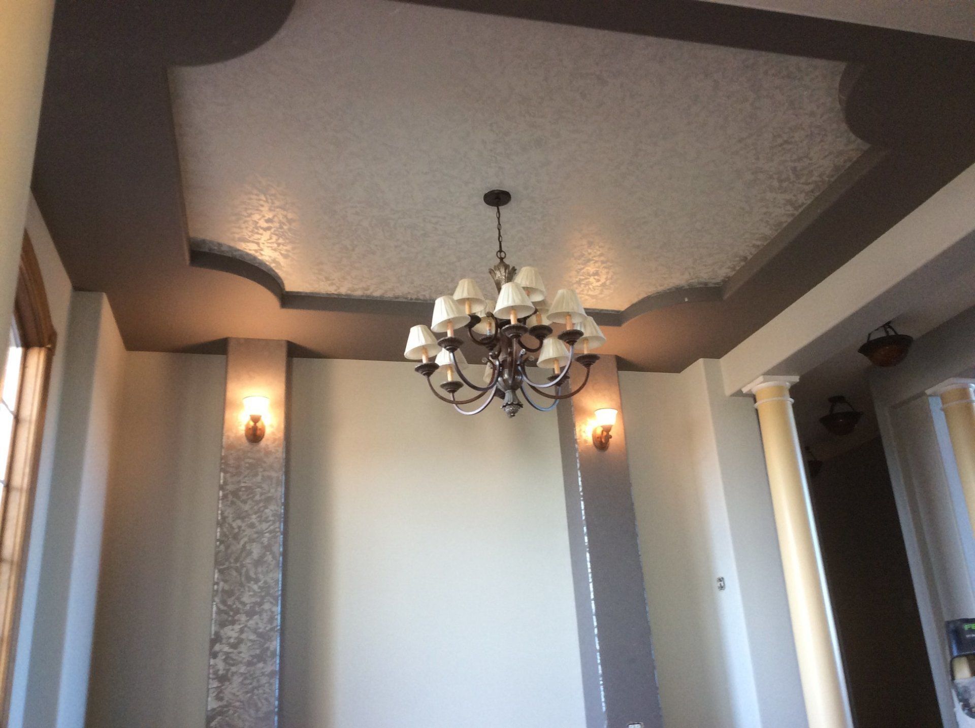 Elegant dining room ceiling with chandelier, tray ceiling, and wall sconces