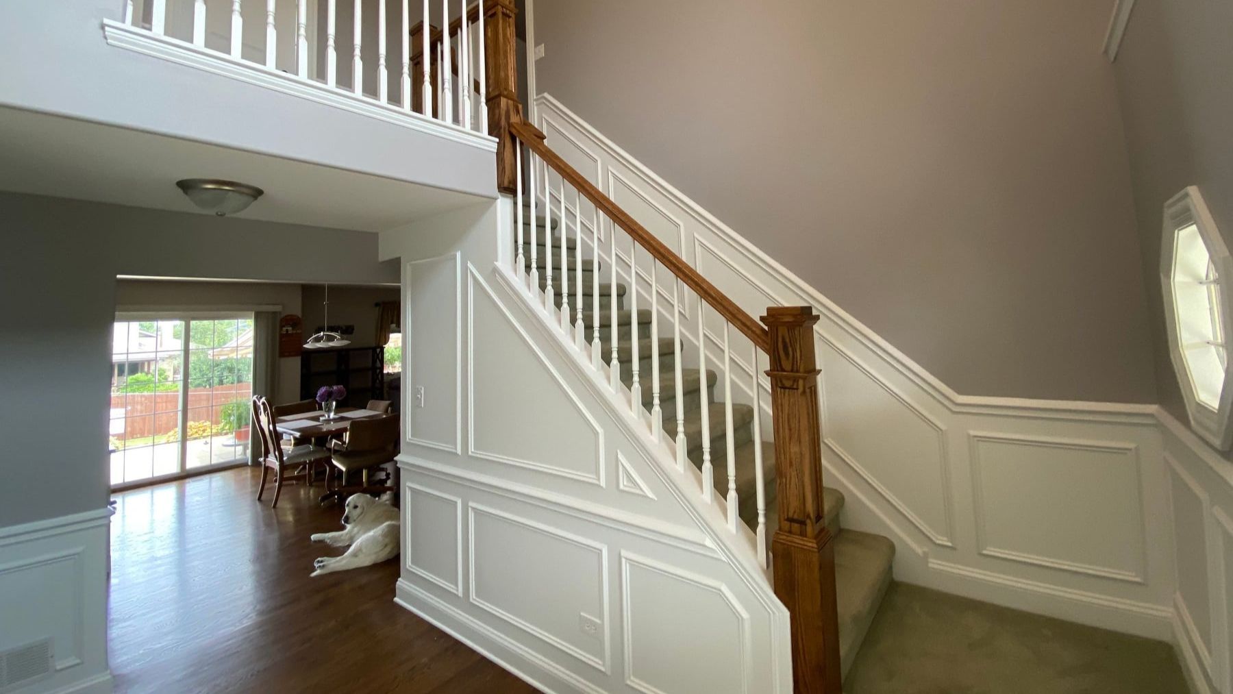 Interior foyer with a staircase, white wainscoting, wood handrail, and hardwood floors leading to a living area
