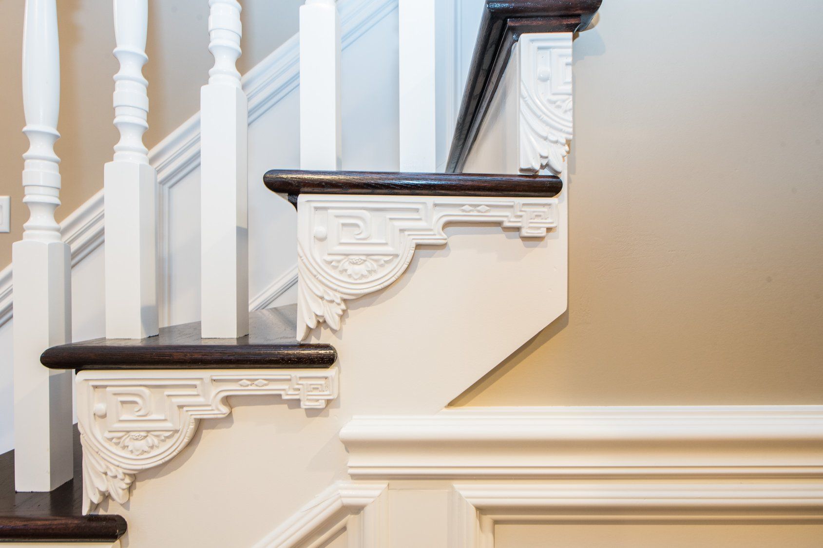 White staircase with dark wooden treads and ornate cream trim in a bright interior