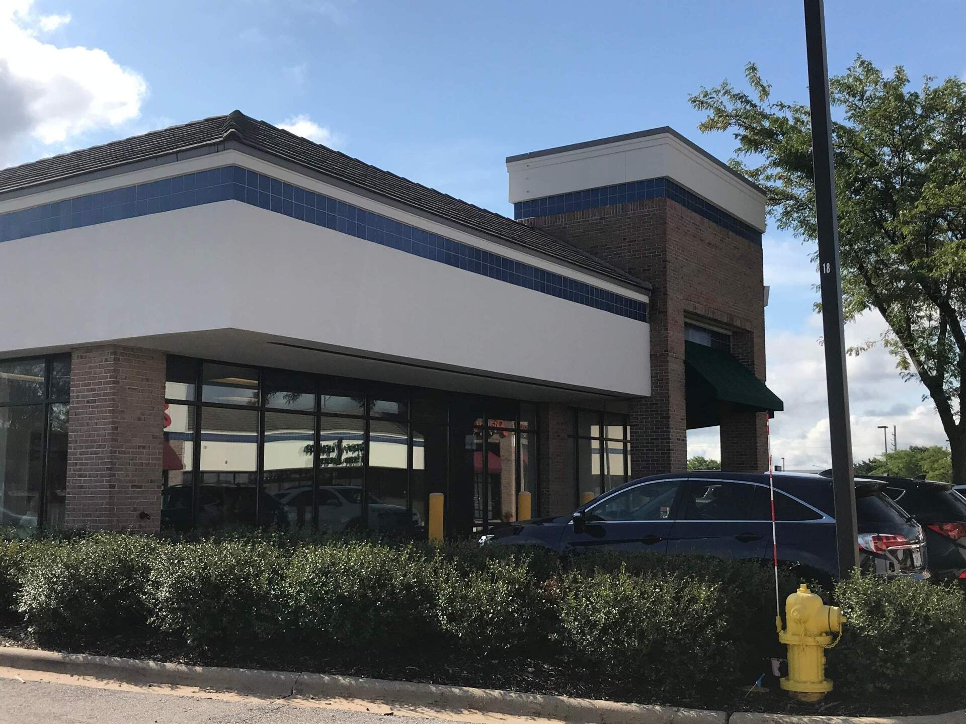 Storefront with brick and white exterior, dark windows, parked cars, and a yellow fire hydrant in front