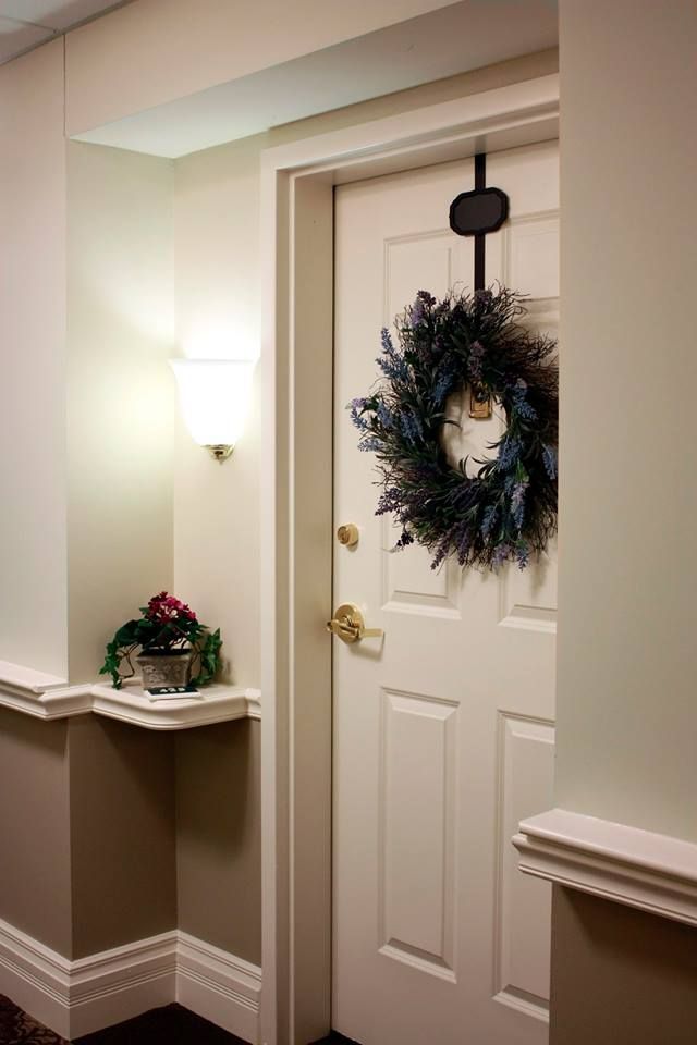 Decorated apartment door with a wreath, wall sconce, and small plant on a shelf in a beige hallway