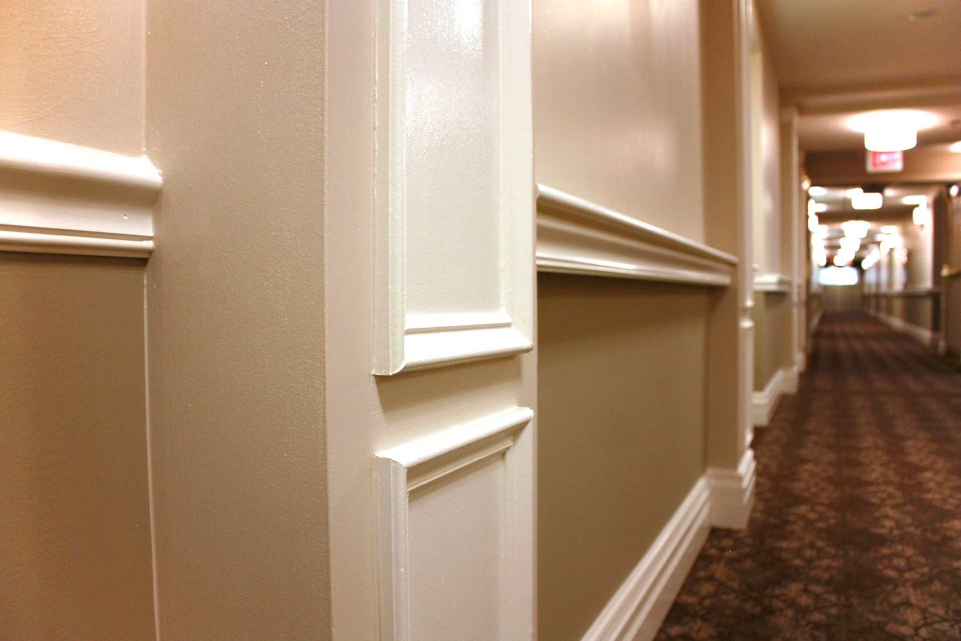 Long hotel hallway with beige walls, white trim, and patterned carpet receding into the distance