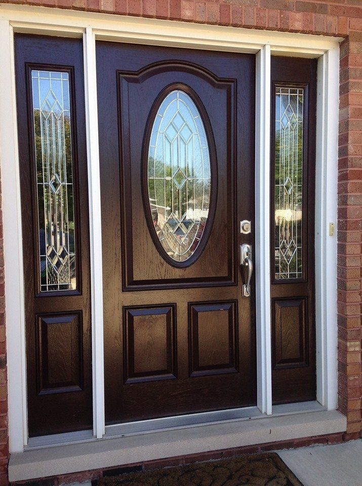 Front entrance with a dark wood front door, oval glass panel, and sidelights framed by brick.