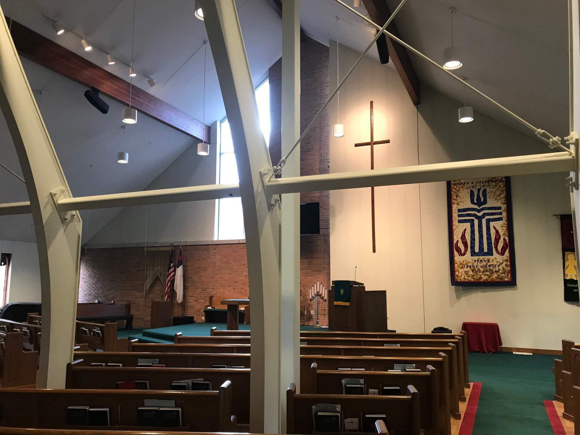 Interior of a church sanctuary with wooden pews, a pulpit, and a cross on the front wall