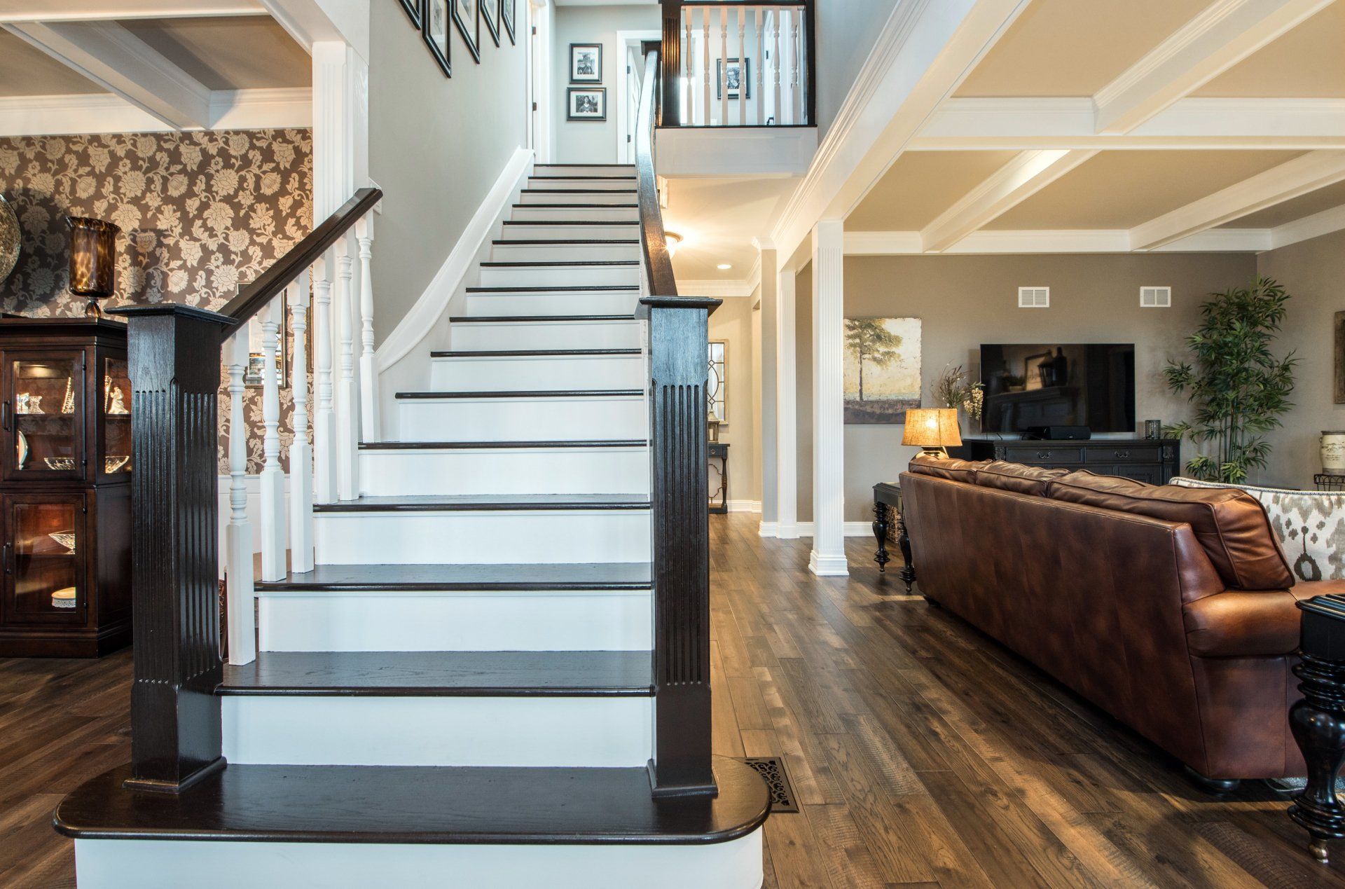 Open staircase in a modern living room with wood floors, leather sofa, and stone fireplace.