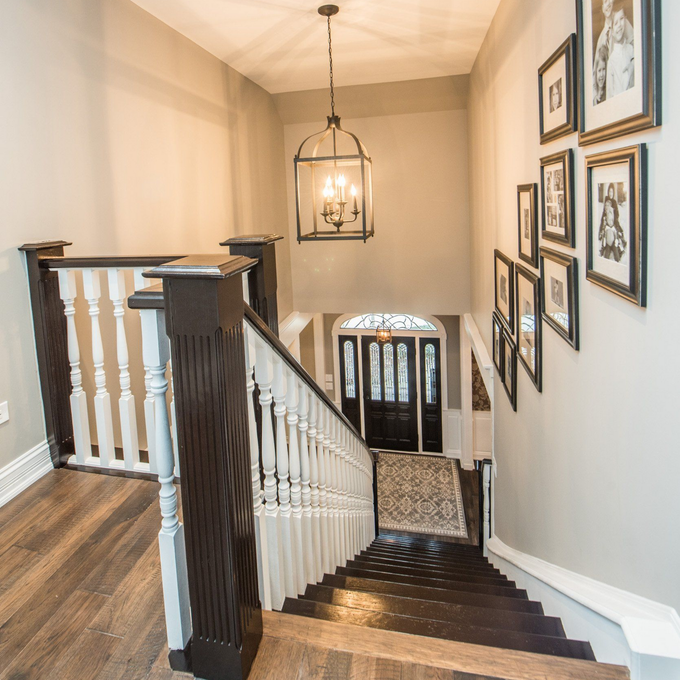 Staircase landing with dark wood banister, white spindles, hanging lantern, and framed art on beige walls