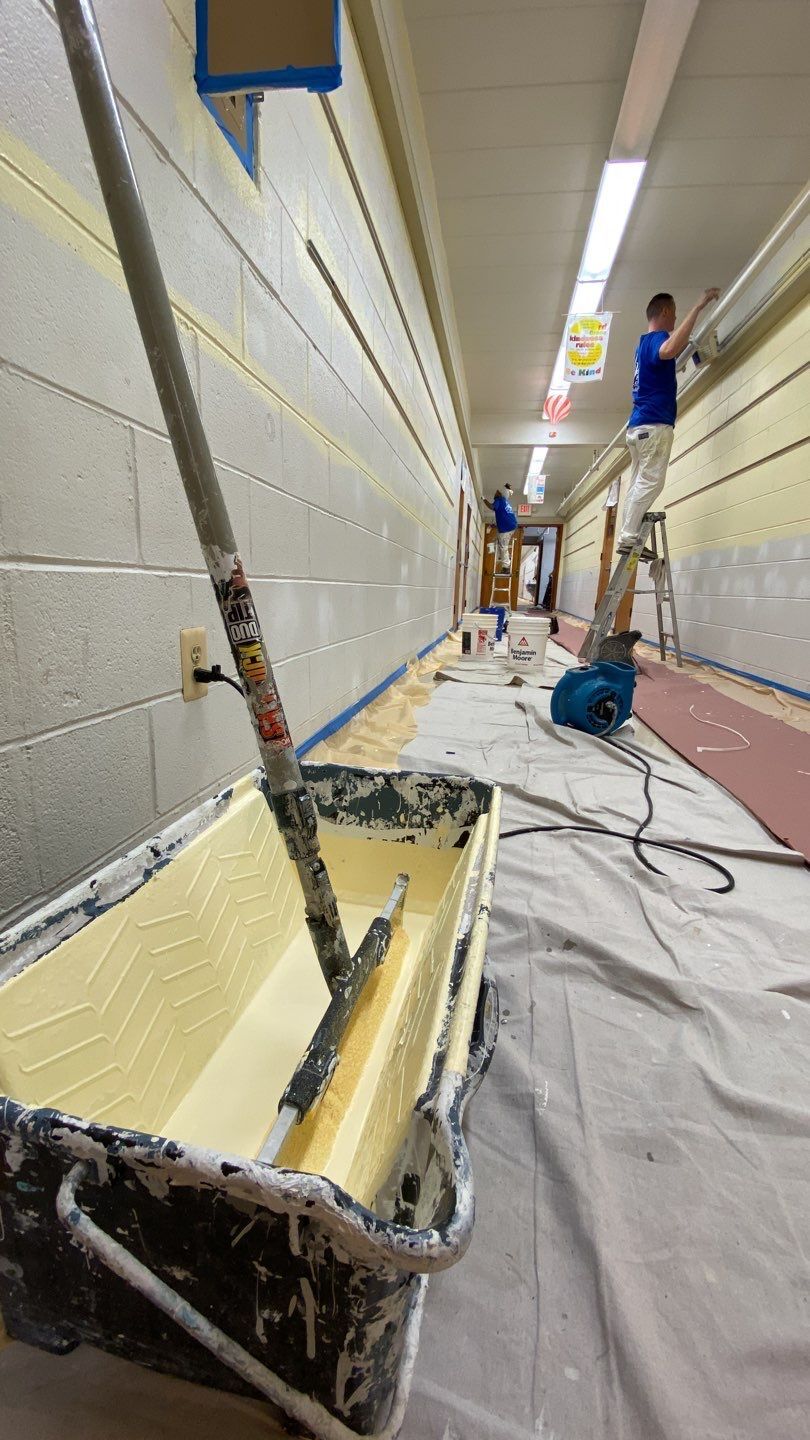 Paint roller and paint tray in a narrow hallway as workers paint the walls and floor protected by drop cloths.