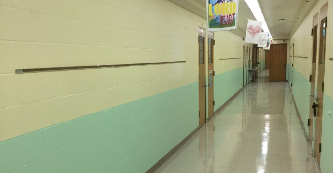 Empty school hallway with mint-green walls, open doors, and polished floor under fluorescent lights