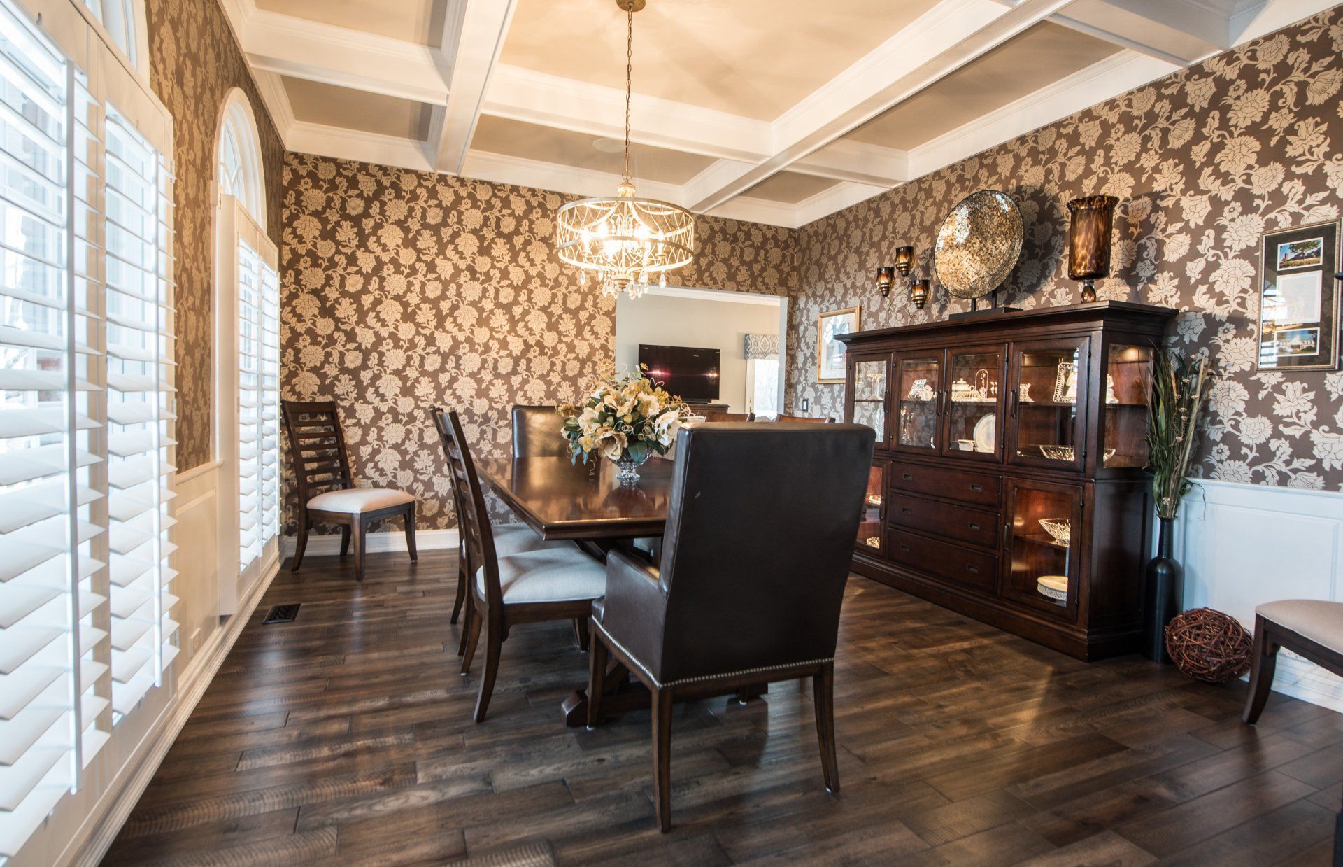 Elegant dining room with dark wood table, black chairs, patterned wallpaper, and large china cabinet