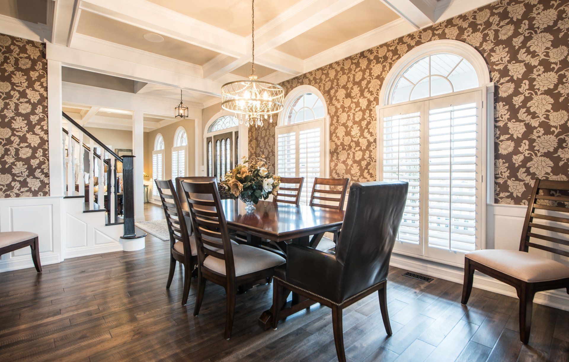 Elegant dining room with dark wood table, chandelier, patterned wallpaper, and large arched windows