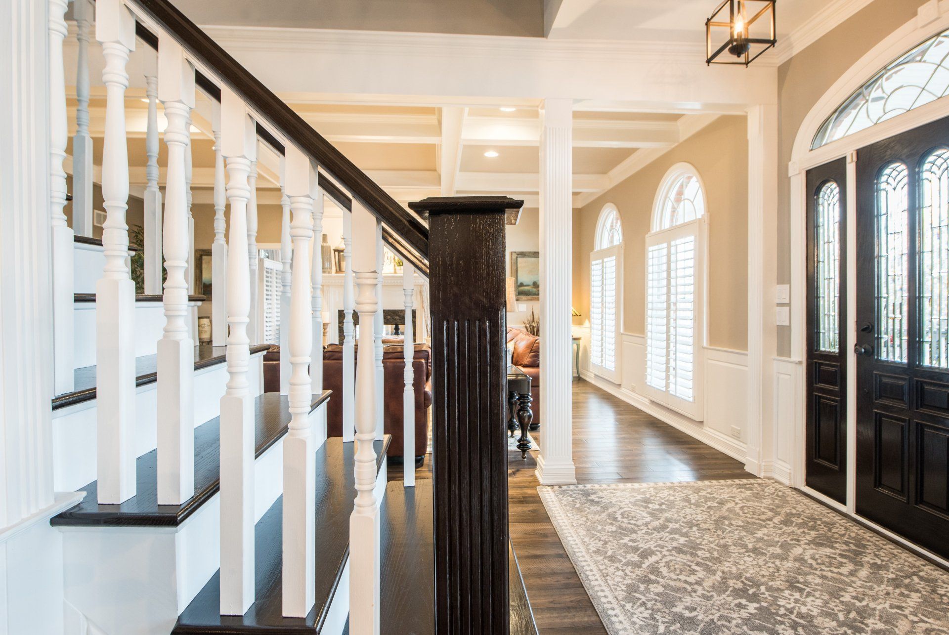 Bright foyer with staircase, black front doors, arched windows, and patterned runner rug