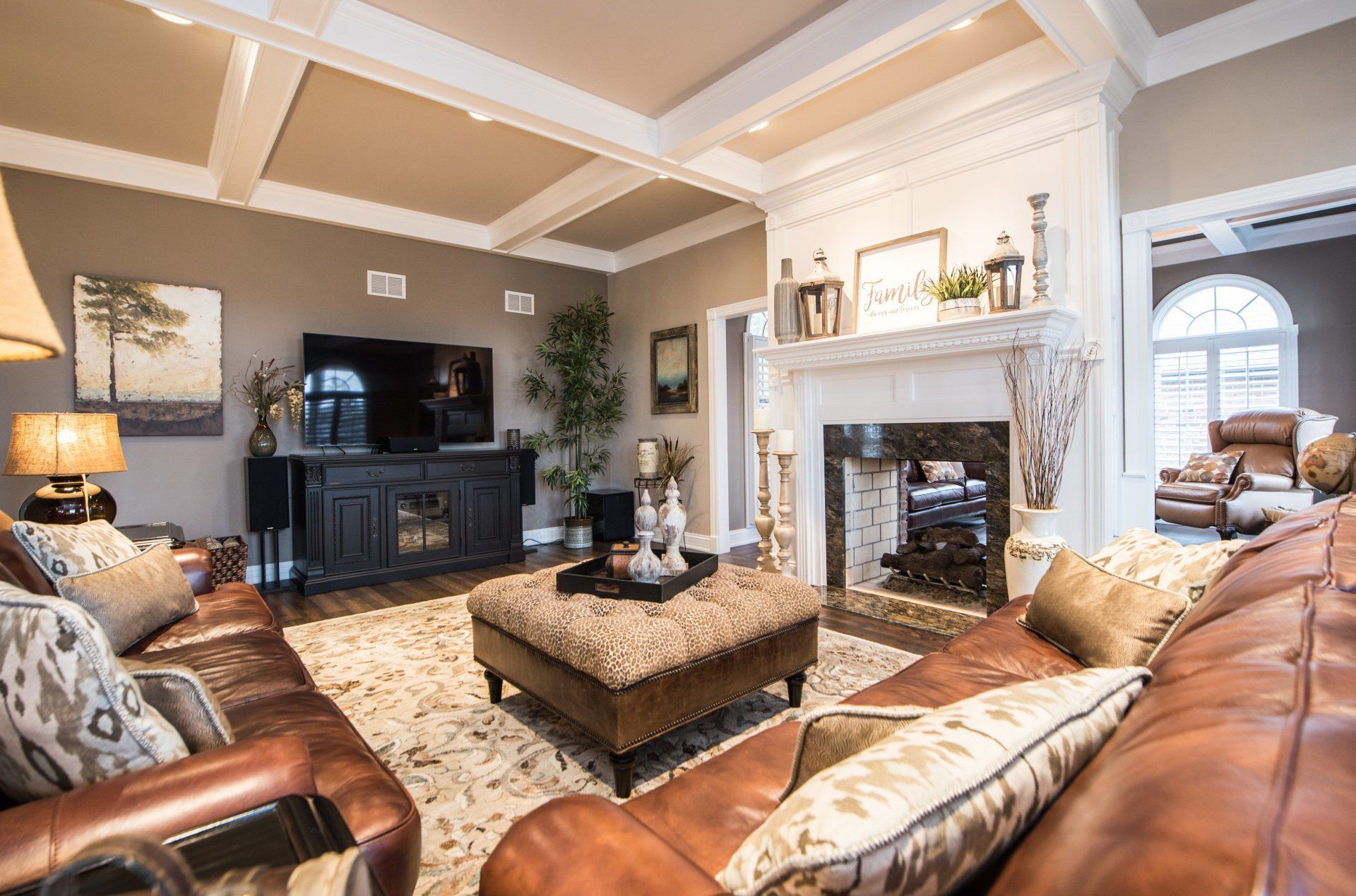 Elegant living room with leather sofas, tufted ottoman, TV, and fireplace under a vaulted ceiling