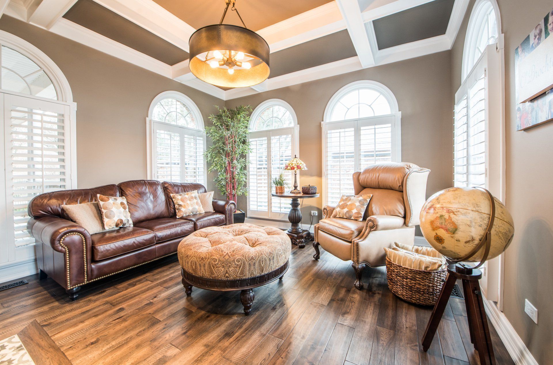 Bright living room with leather sofa, armchair, ottoman, globe, and arched windows in sunlight