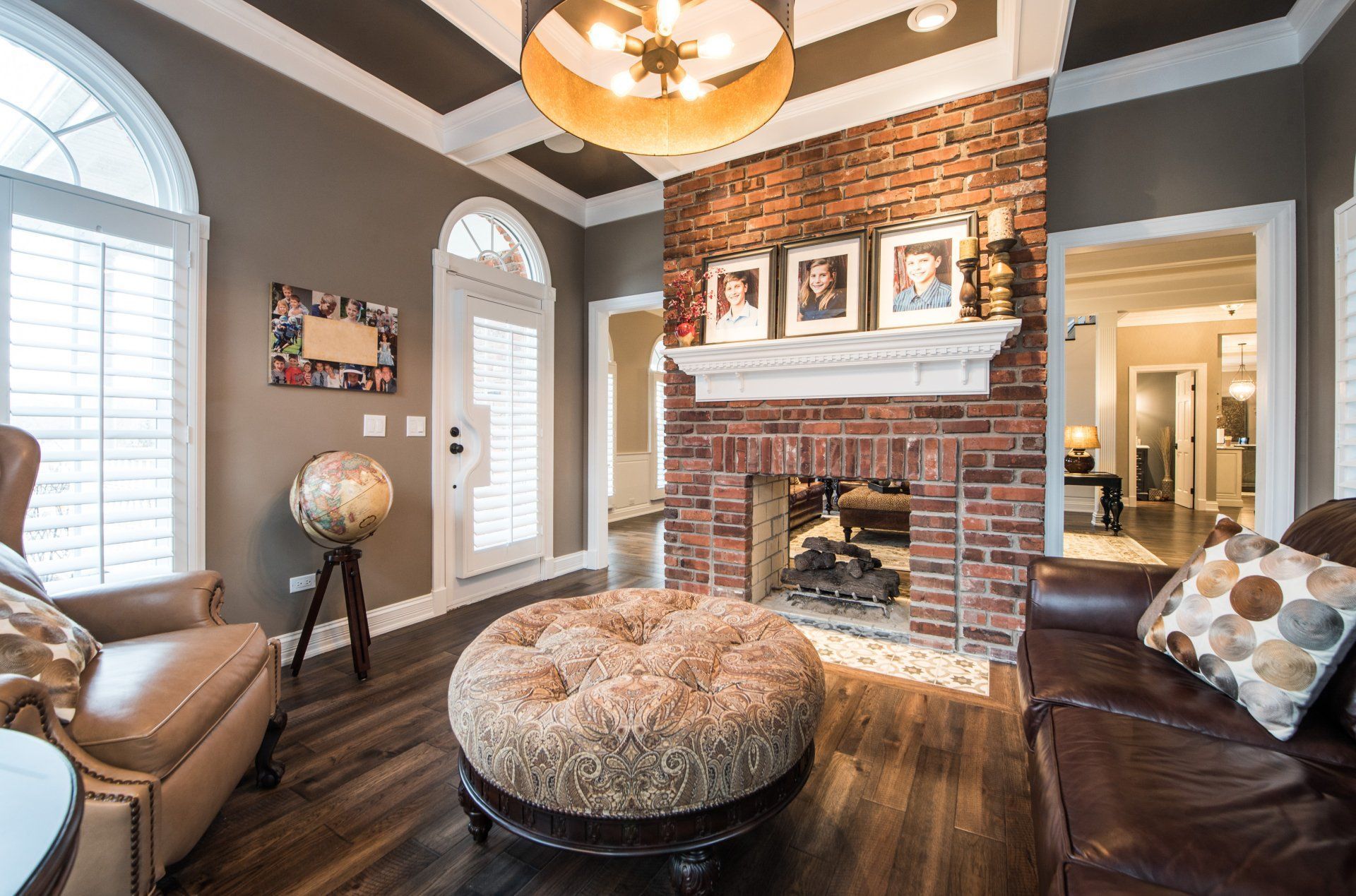 Cozy living room with brick fireplace, brown leather seating, and a large window with white shutters