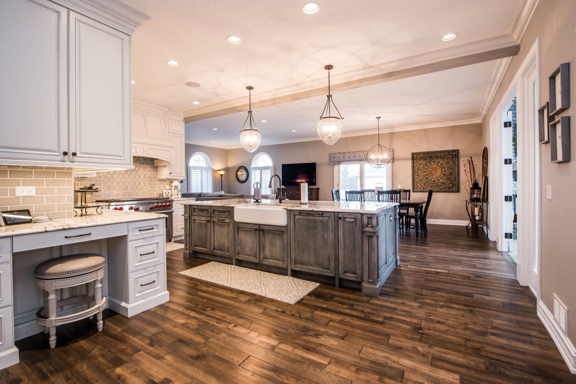 Open-plan kitchen with gray island, white cabinets, wood floors, and pendant lights