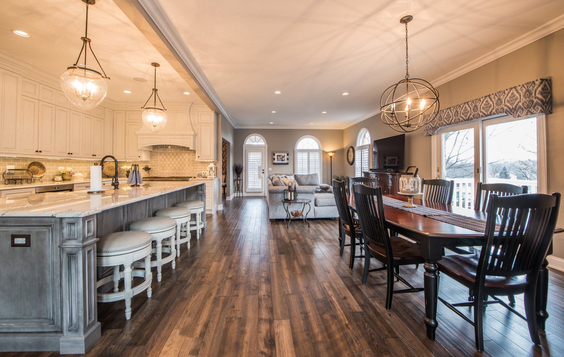 Open-concept kitchen and dining area with gray cabinets, wood floors, and a large dining table by windows
