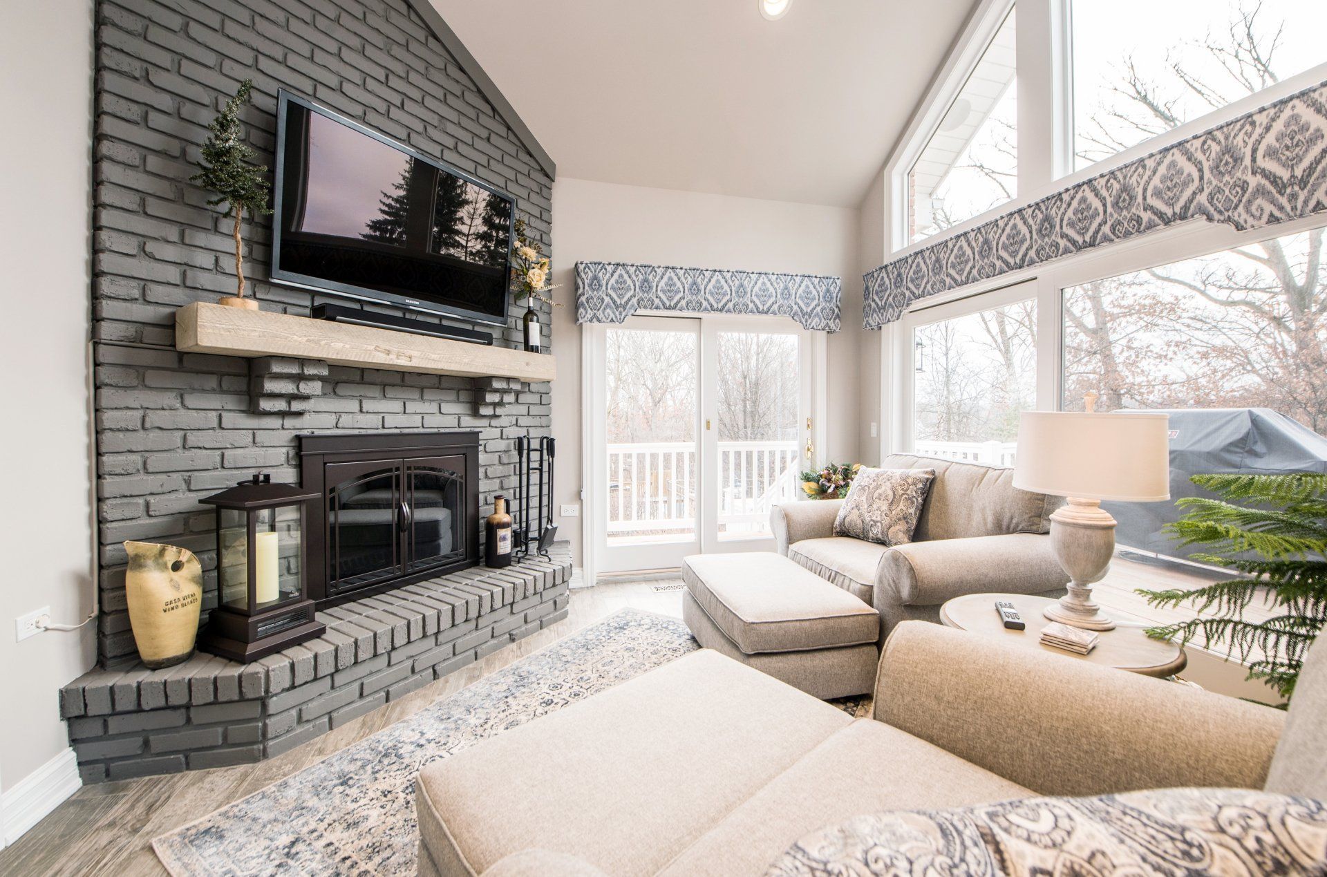 Bright living room with gray brick fireplace, wall-mounted TV, sectional sofa, and large windows