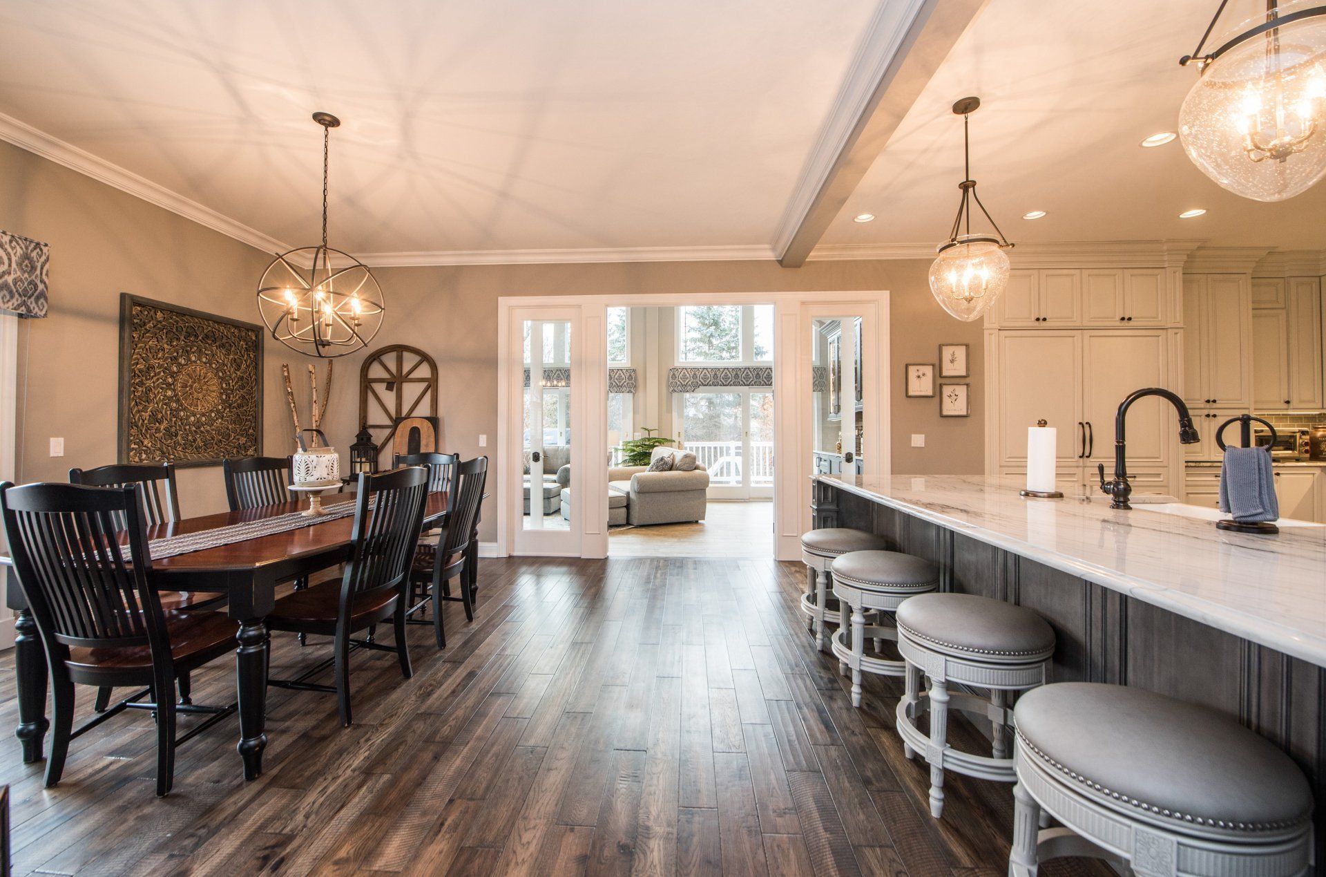 Open-concept kitchen and dining room with dark wood floors, island stools, and a table by French doors.