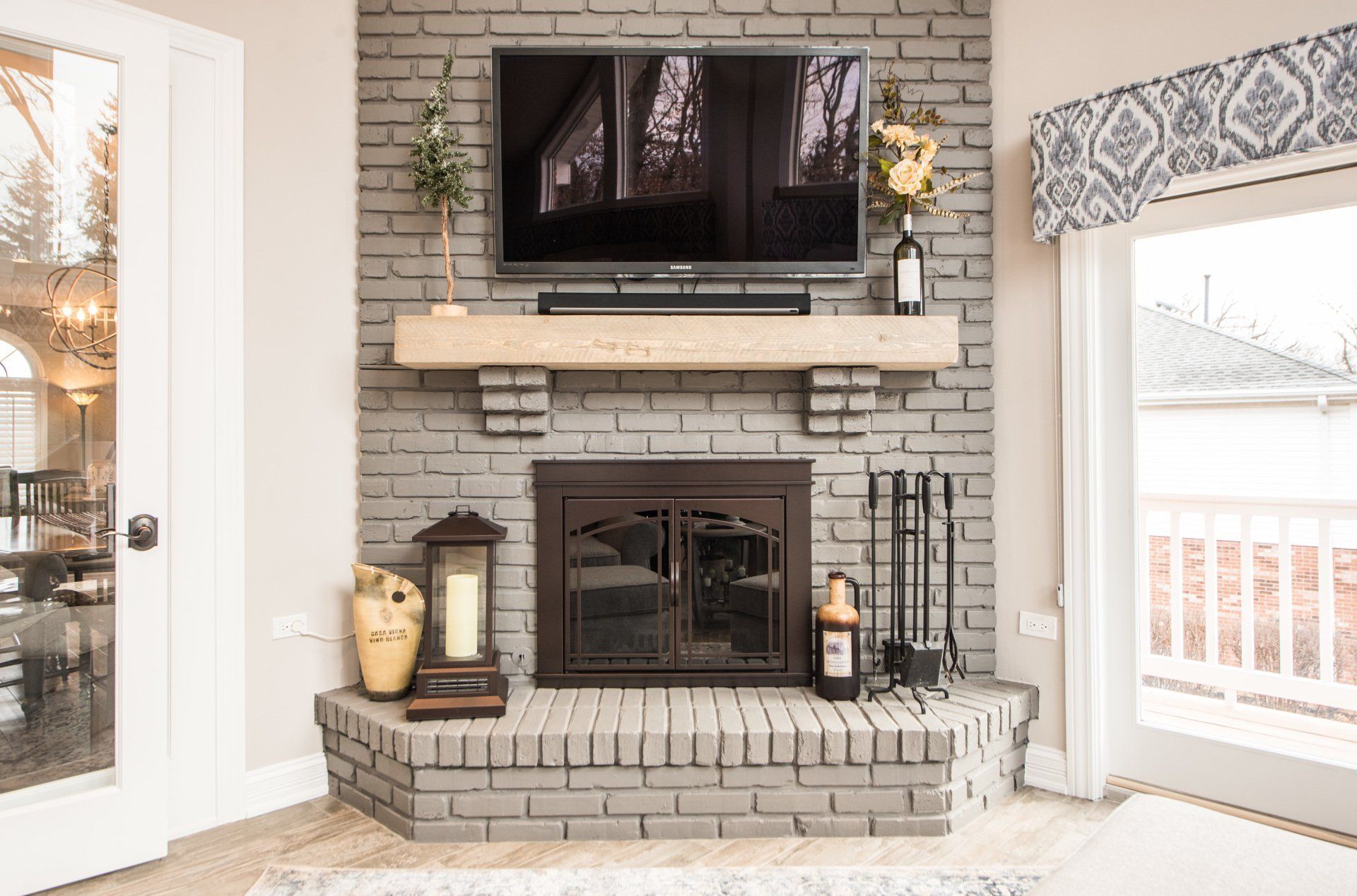 Stone fireplace with wall-mounted TV, mantel decor, and large windows in a bright living room