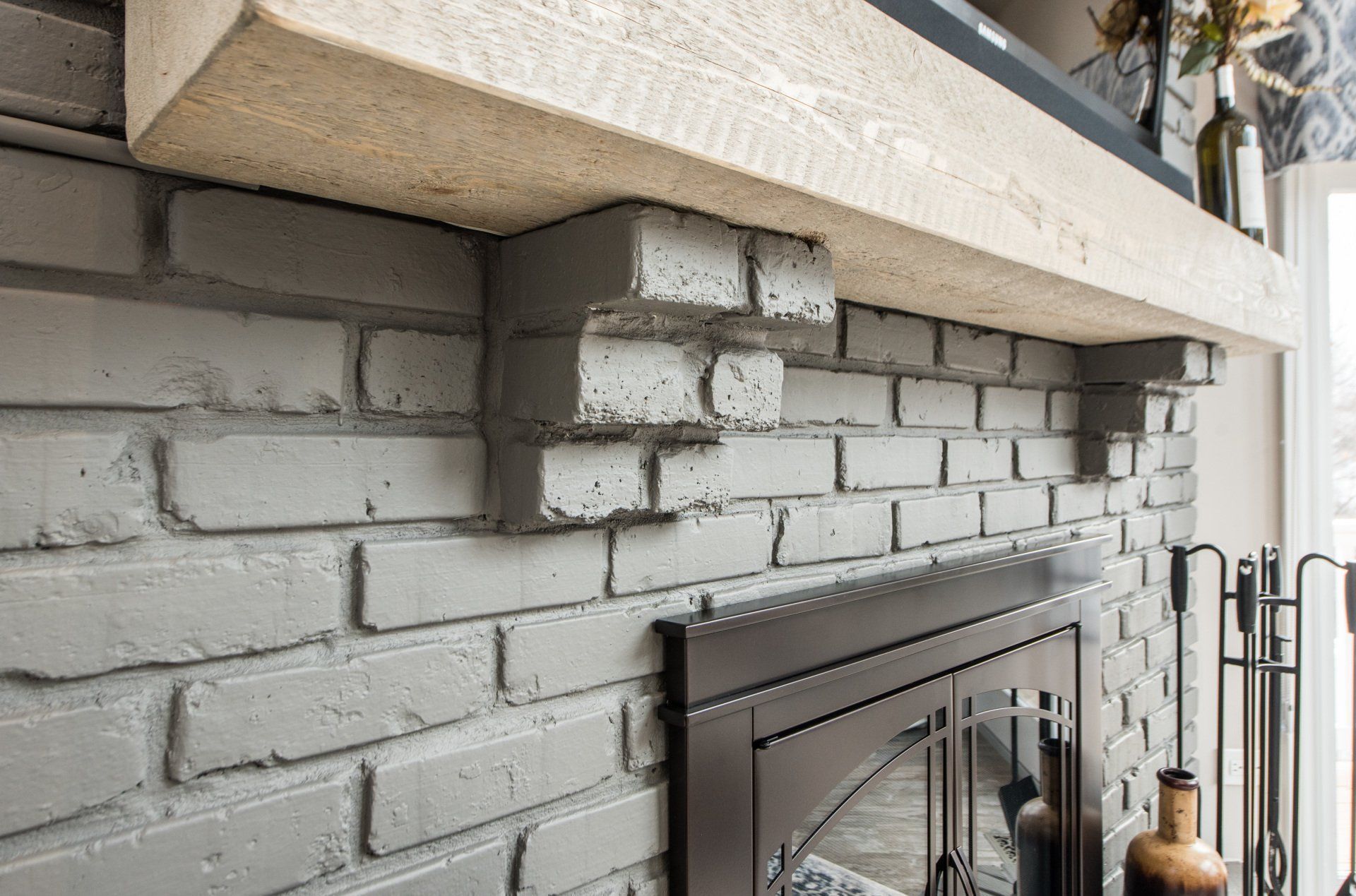 White painted brick fireplace with a dark metal firebox and a light wood mantel shelf