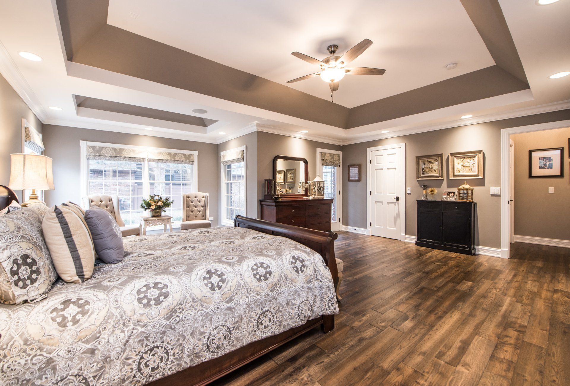 Elegant bedroom with a four-poster bed, tray ceiling, hardwood floors, and dark wood furniture