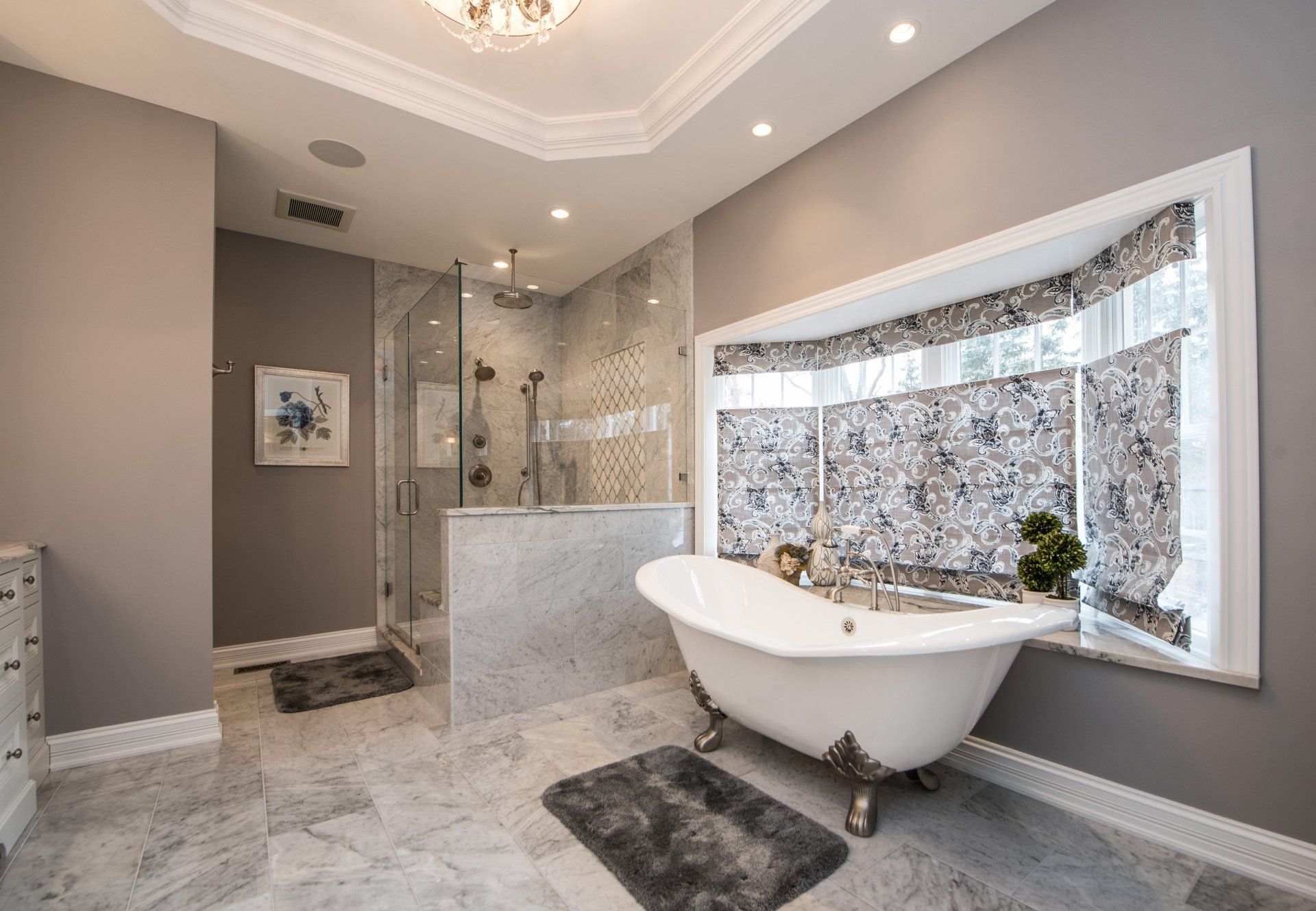 Elegant bathroom with freestanding tub, marble tile, glass shower, and large window with patterned curtain