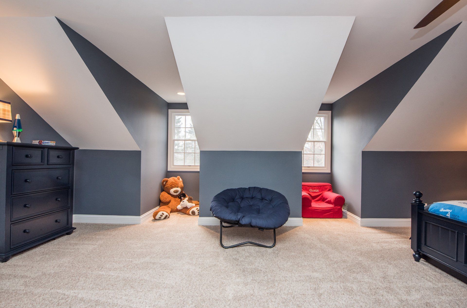 Attic room with slanted gray walls, two windows, and a central blue chair on carpet.