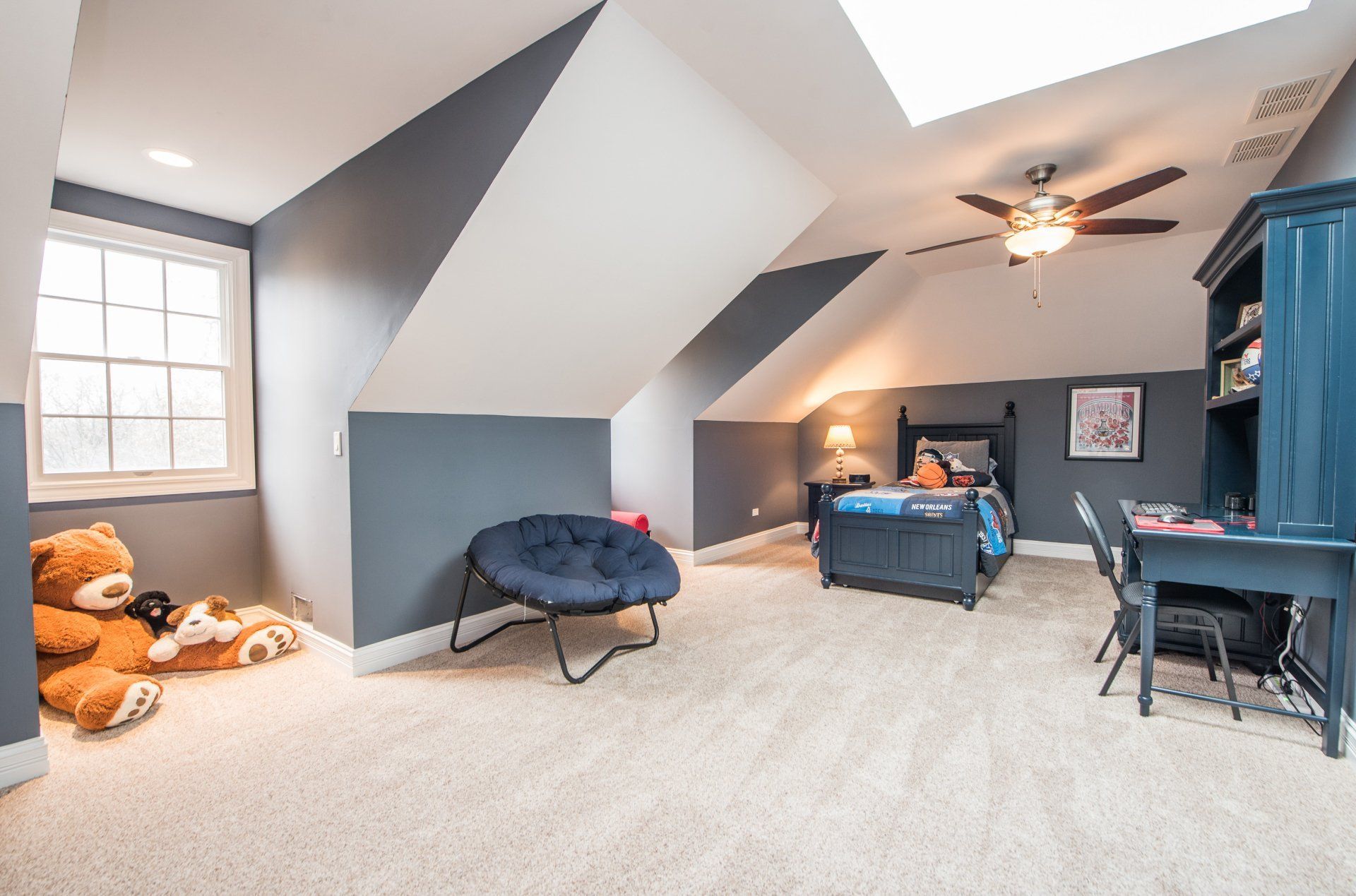 Bright attic bedroom with twin beds, blue walls, skylights, a chair, and stuffed animals near the window