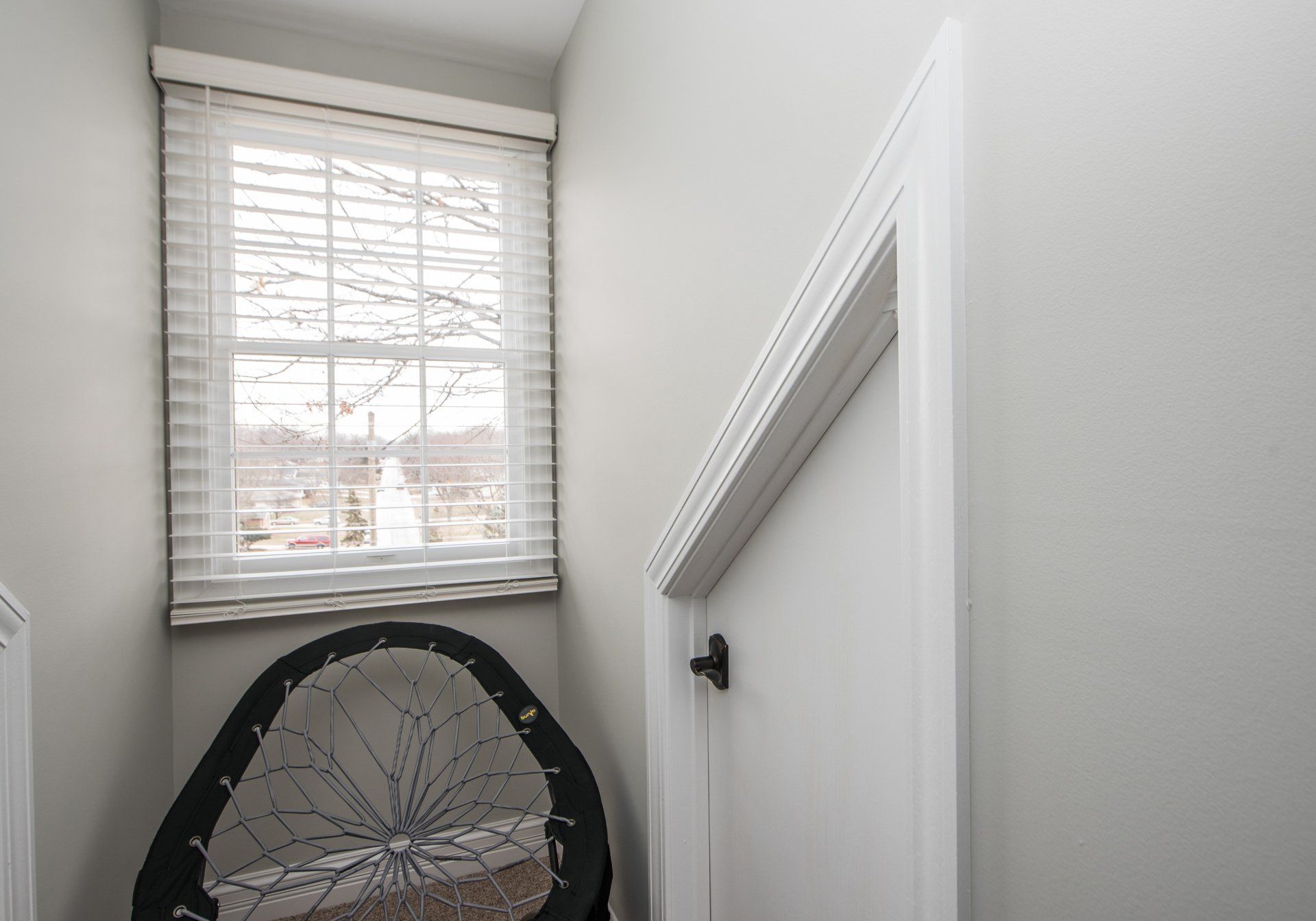 Narrow stairwell with white walls, window blinds, and a black chair or bike wheel at the bottom