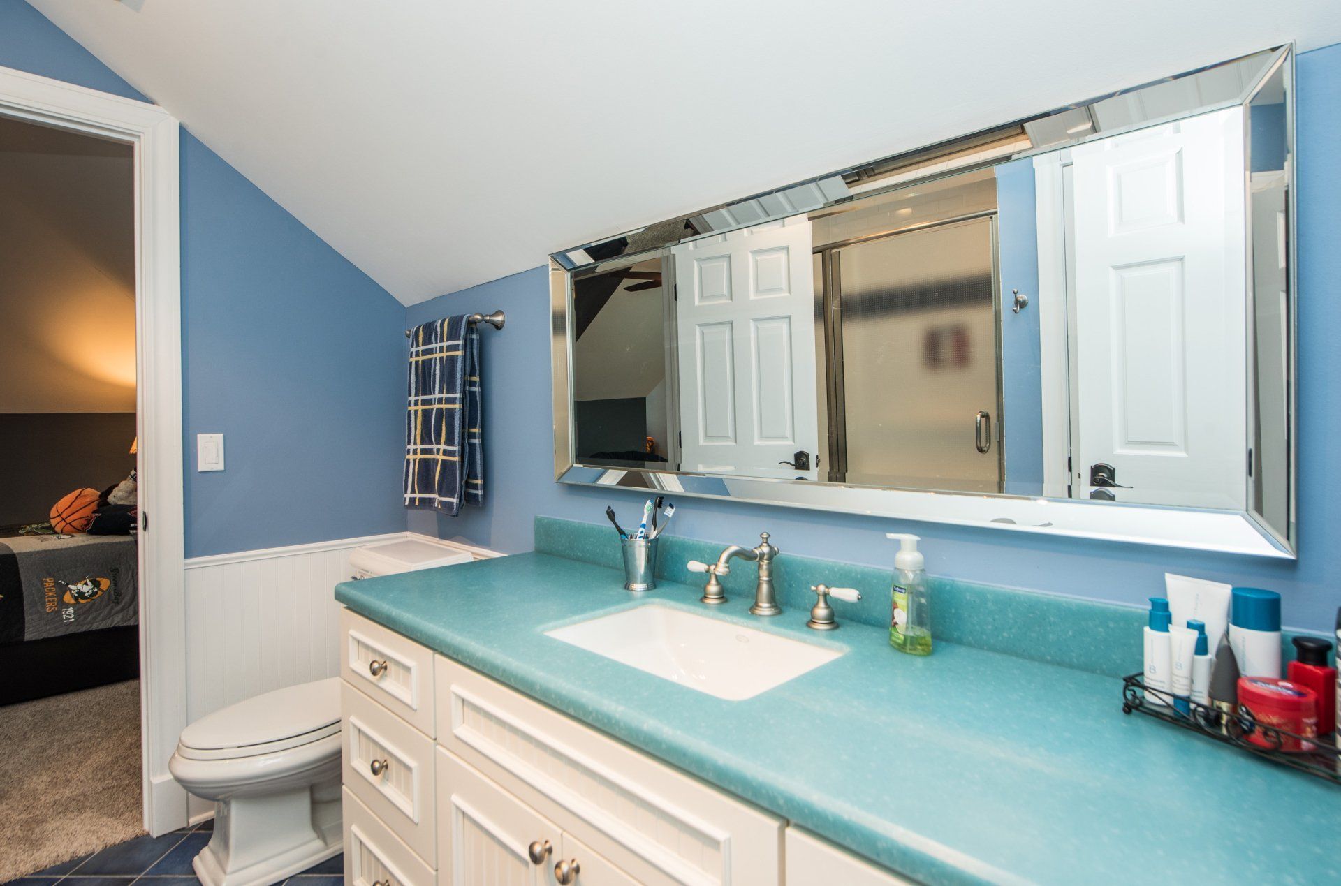 Bright bathroom with blue walls, white vanity, turquoise countertop, and large mirrored medicine cabinet.