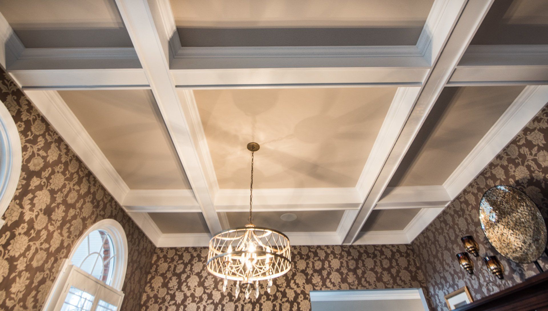 Coffered ceiling with white beams, warm pendant light, and patterned wallpaper in a room