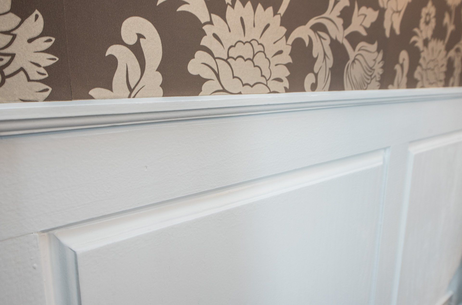 White wainscoting beneath patterned floral wallpaper on an interior wall