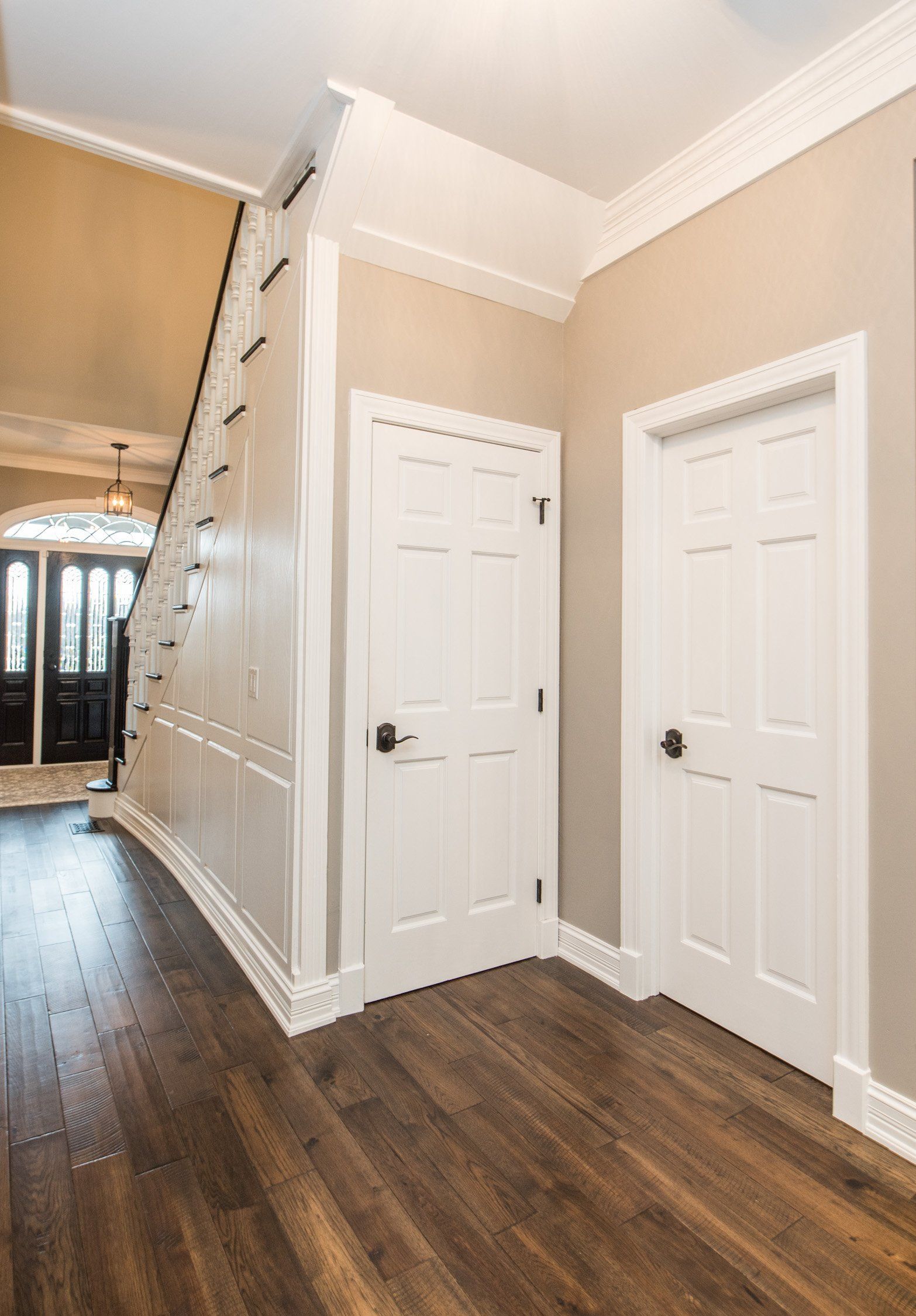 Bright hallway with white doors, beige walls, and dark hardwood floors leading to an entryway
