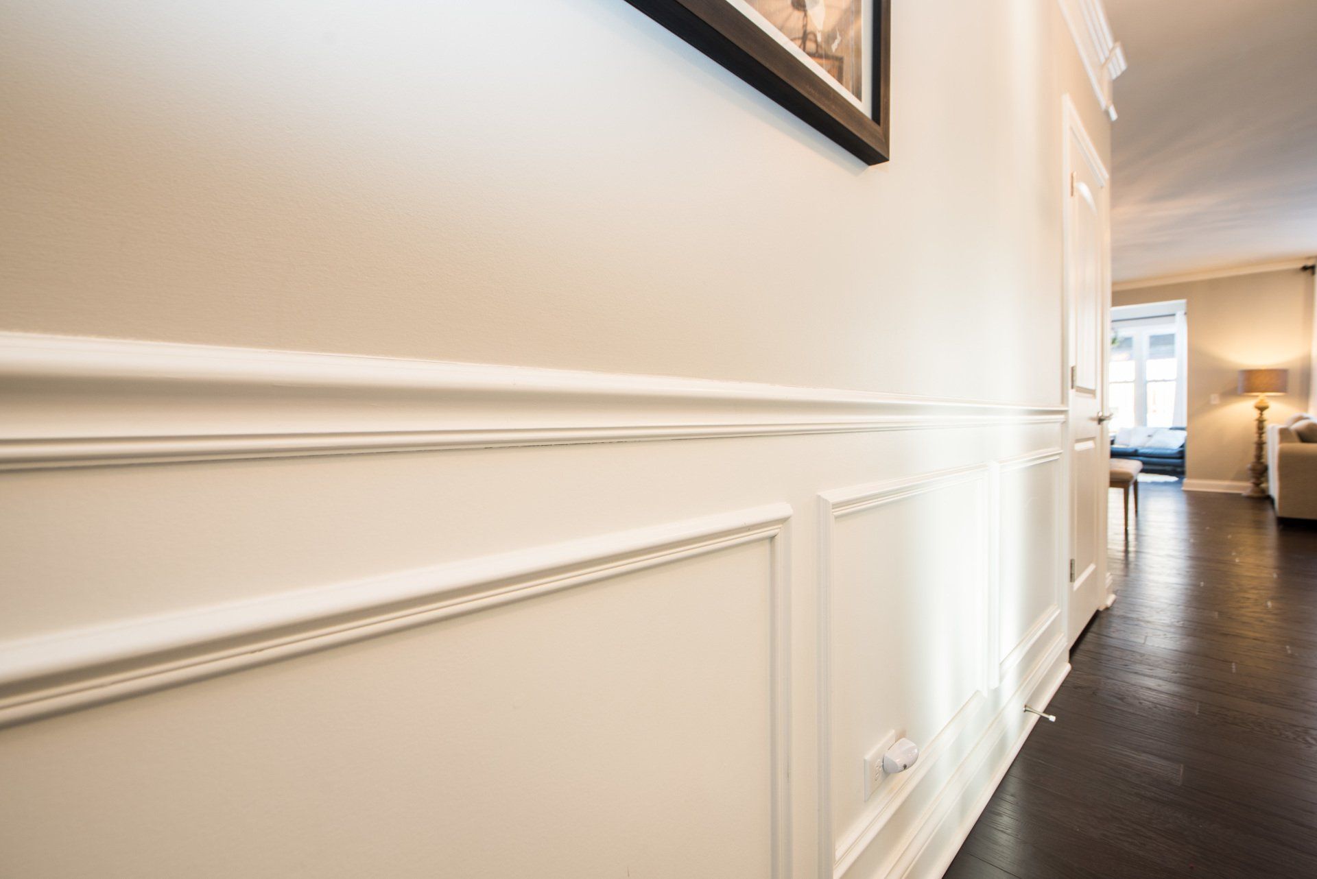 Bright hallway with white wainscoting and dark wood floors leading to a sunlit living room.