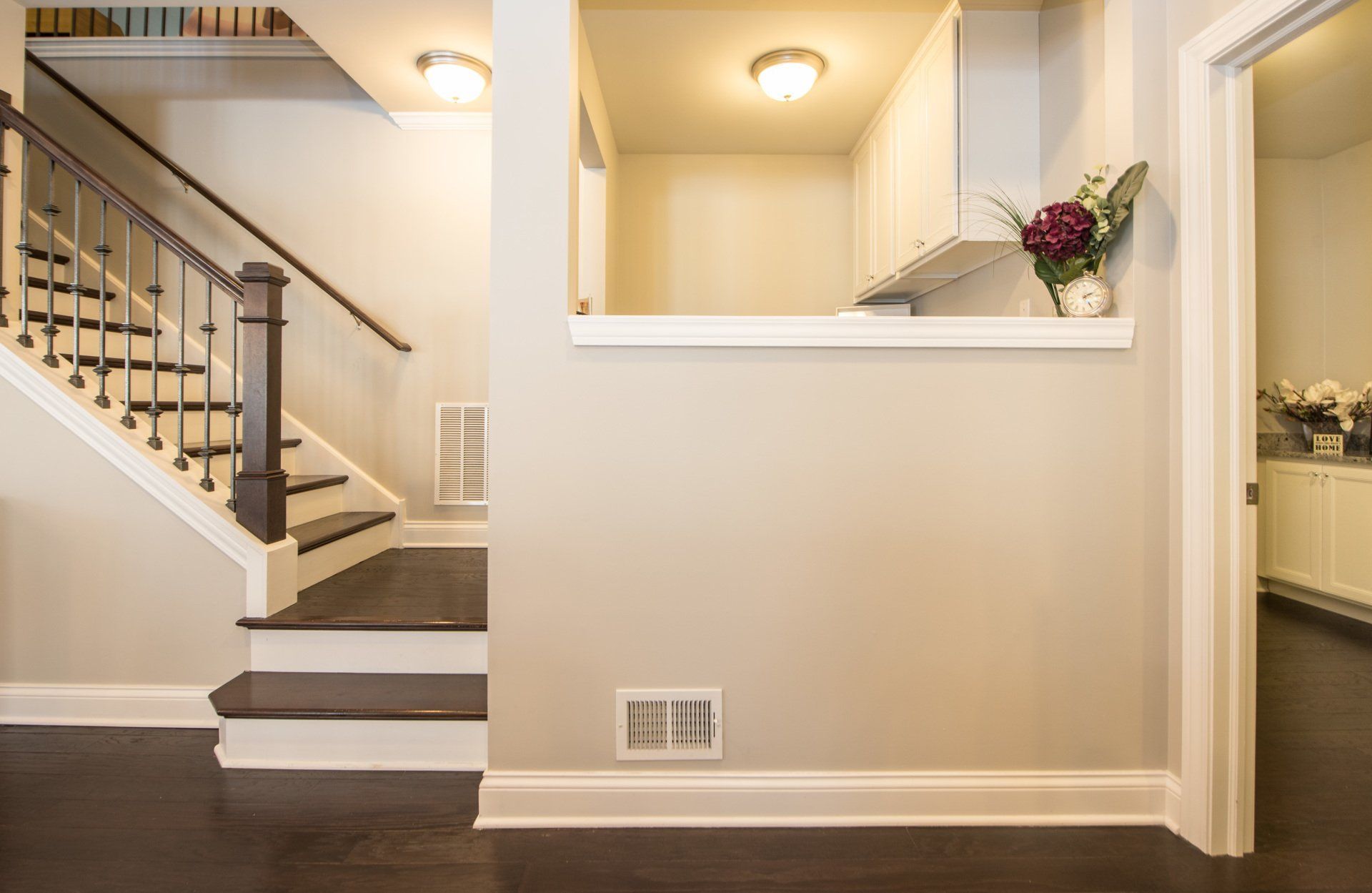 Bright foyer with staircase, white walls, dark wood floors, and a pass-through opening with flowers.