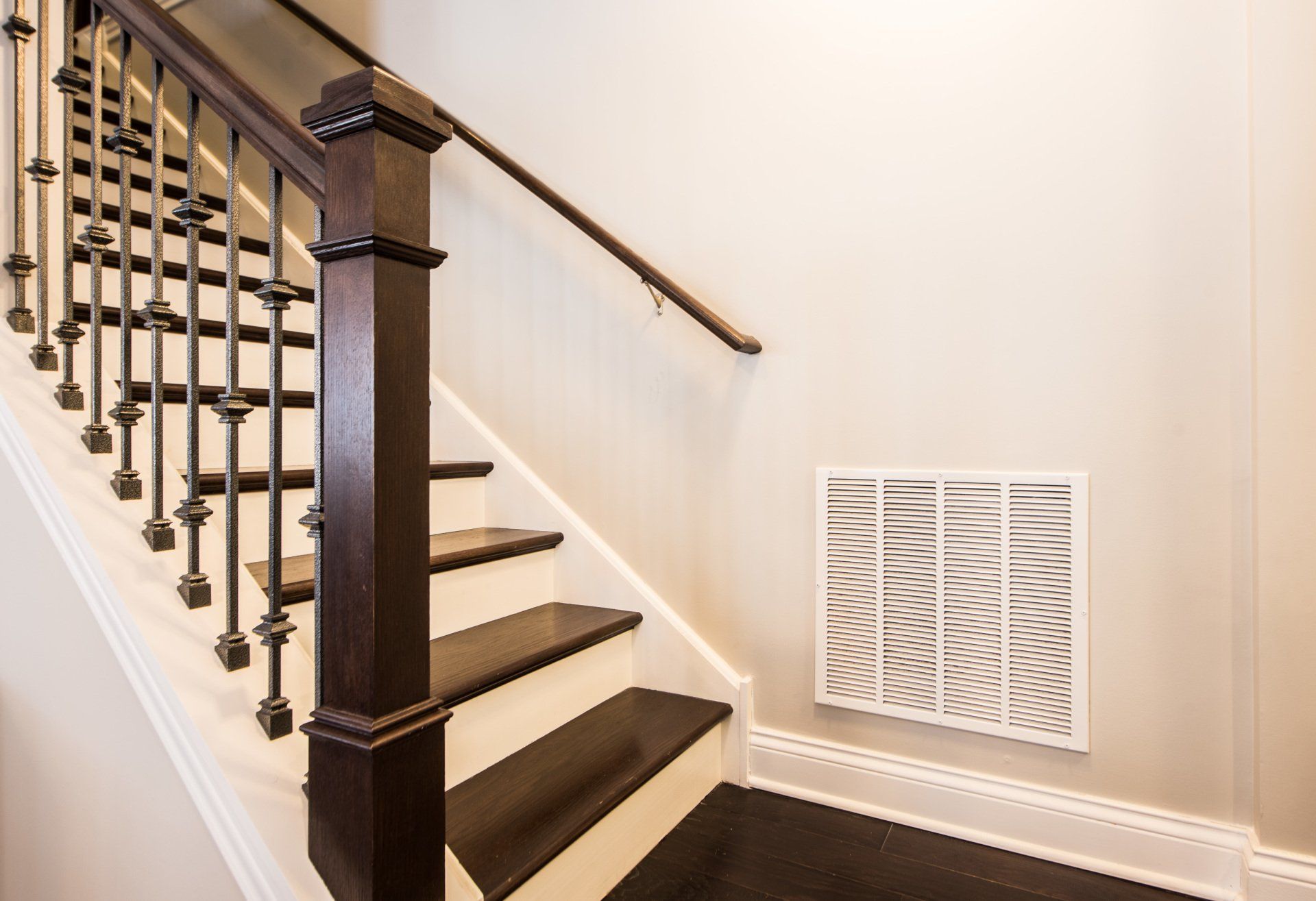 Interior staircase with dark wood railings, white walls, and a floor vent on the landing
