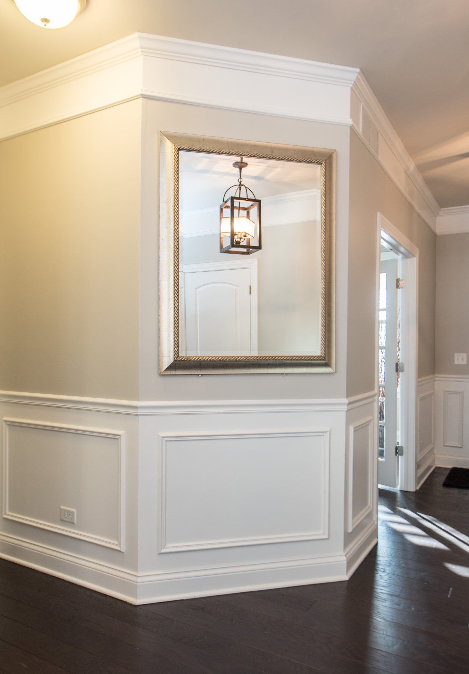 Elegant hallway with white wainscoting, large mirror, hanging lantern, and dark hardwood floors.
