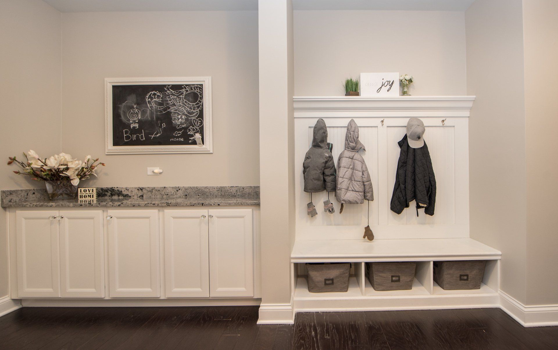 Modern entryway with white cabinets, granite counter, coat hooks, and children’s jackets by a bench.